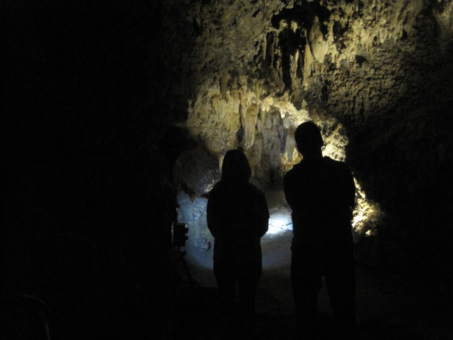 Dimly lit cave with two silhouetted figures facing a rock formation.