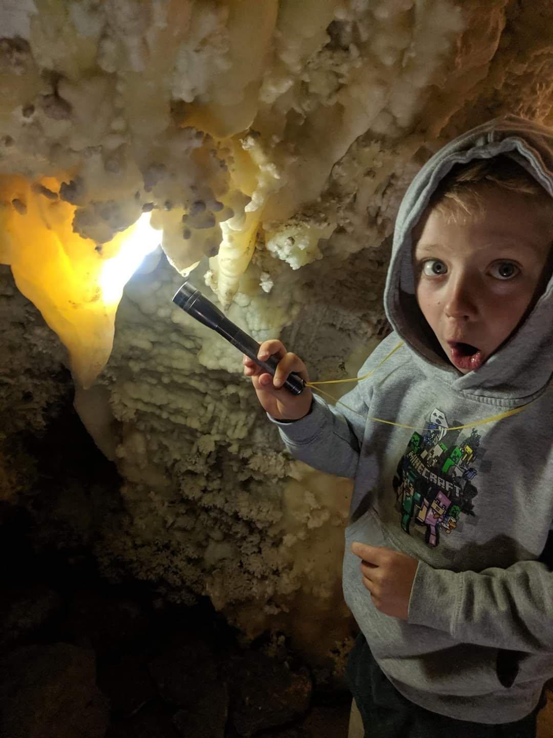 Child in hoodie exploring cave with flashlight, surprised expression.