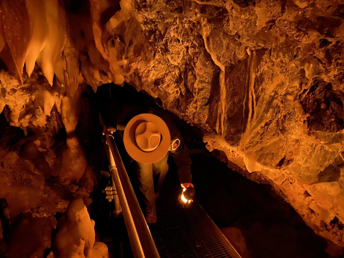 Cave explorer with lantern and hat, surrounded by orange-lit rock formations.