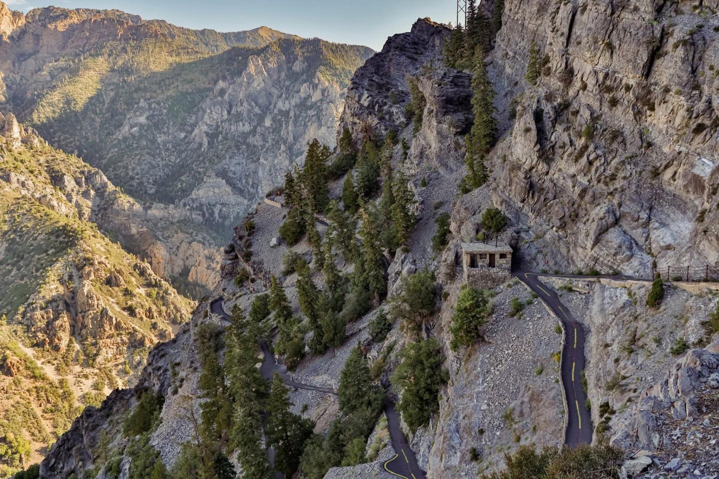 Mountain road winding along a steep cliffside surrounded by pine trees.