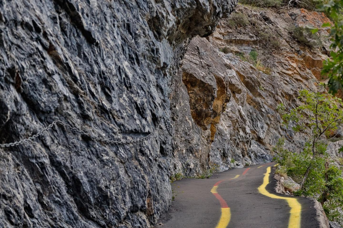 Narrow rocky path with yellow markings curves along a cliff.