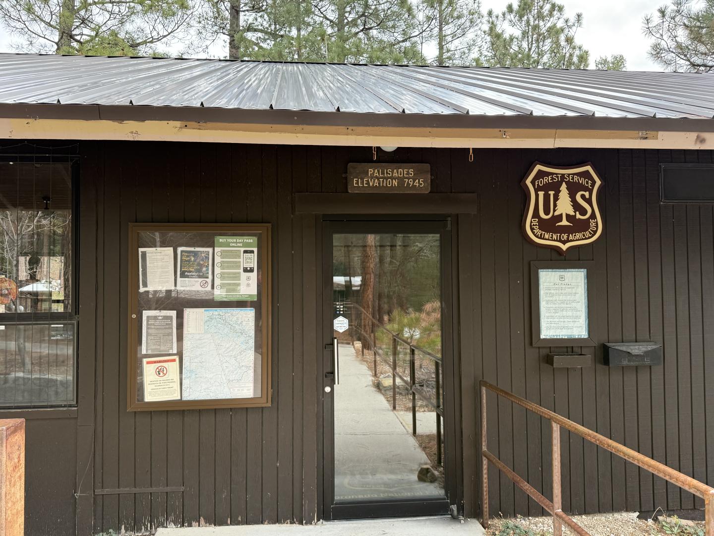 Small brown wooden building with a U.S. Forest Service shield and bulletin board.
