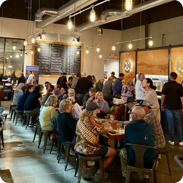 Crowded brewery with people at tables and warm lighting.