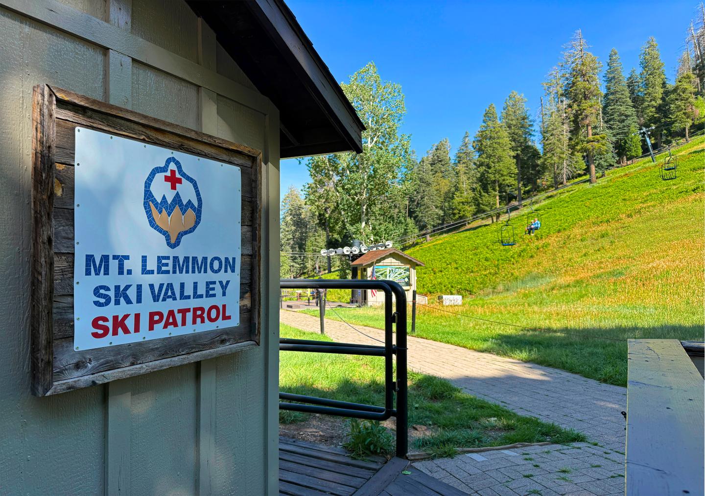 Ski patrol cabin near grassy hill with trees under a clear blue sky.