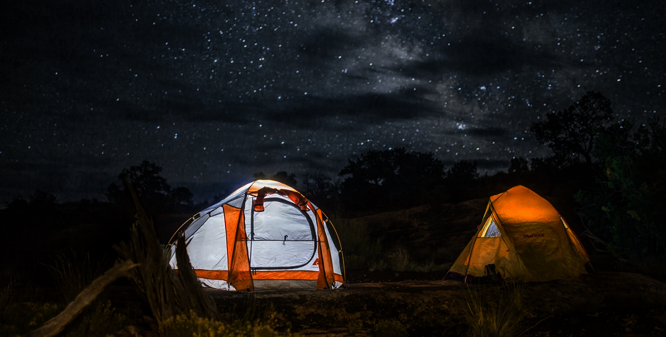 Two lit tents under a starry night sky in a forest clearing.