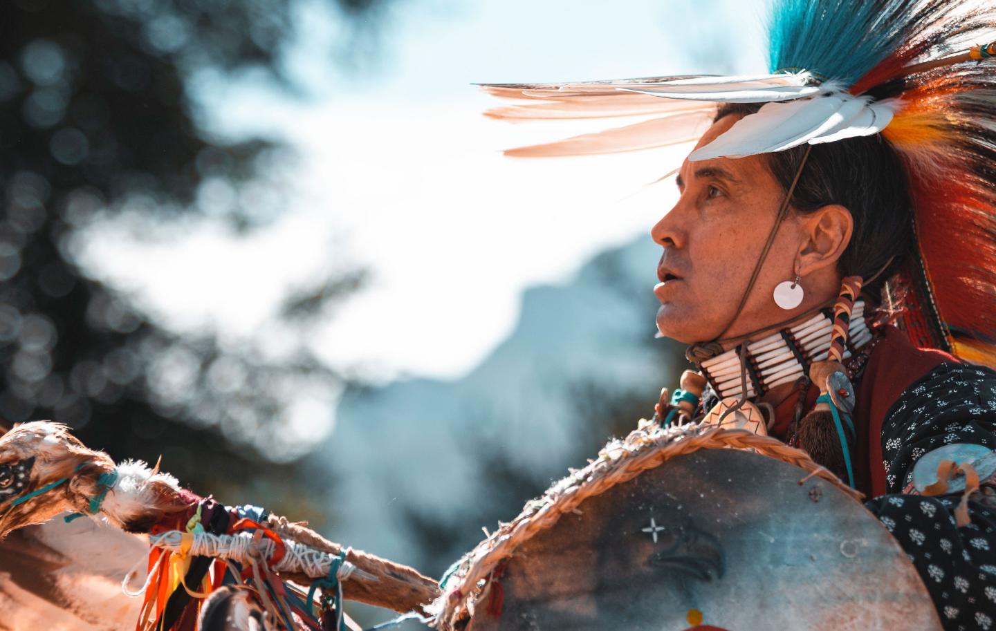 Native American dancer in colorful regalia with feathered headdress, outdoors.