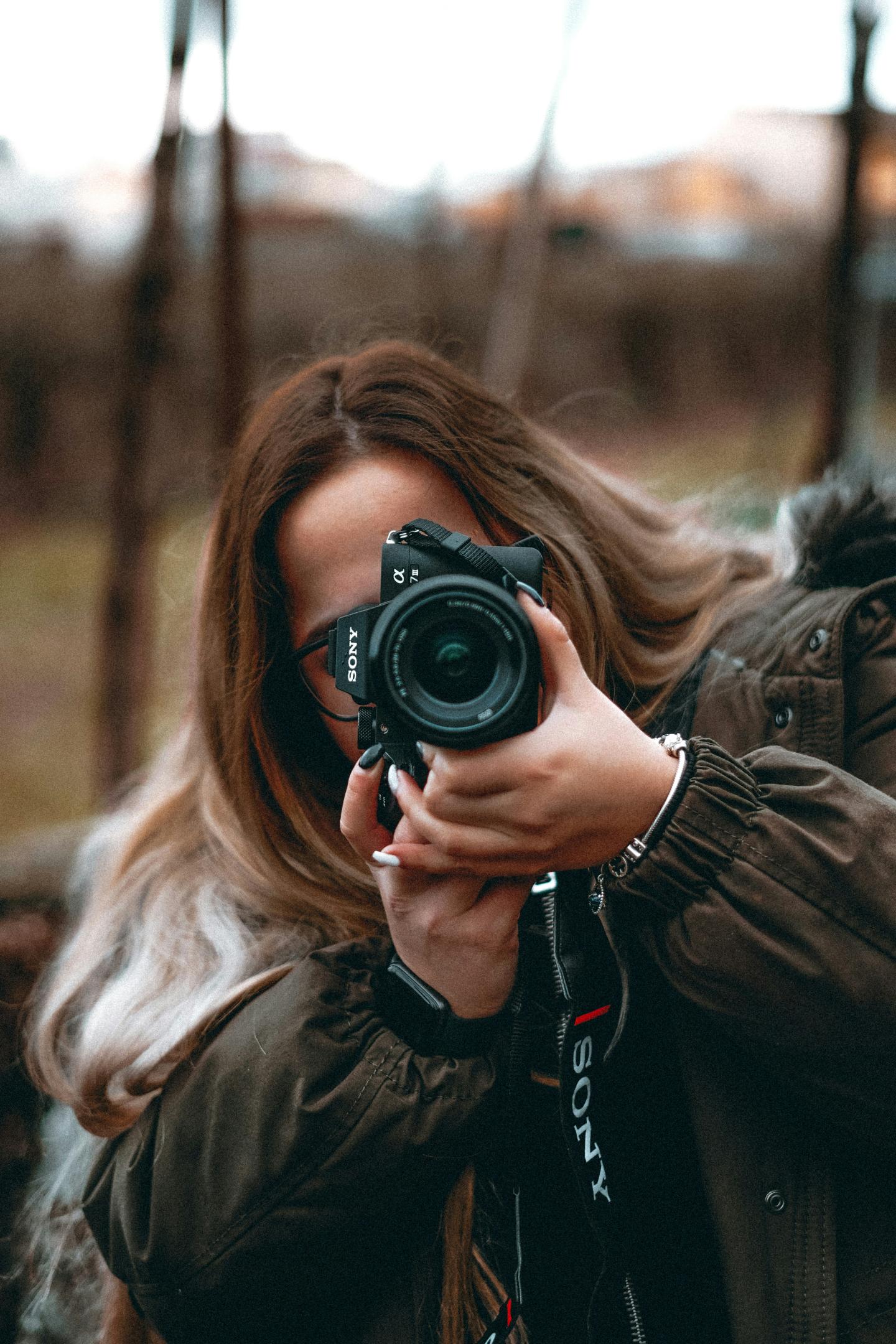 Person with a camera, outdoors, wearing a jacket.