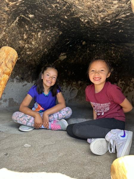 Two children smiling inside a rocky shelter.