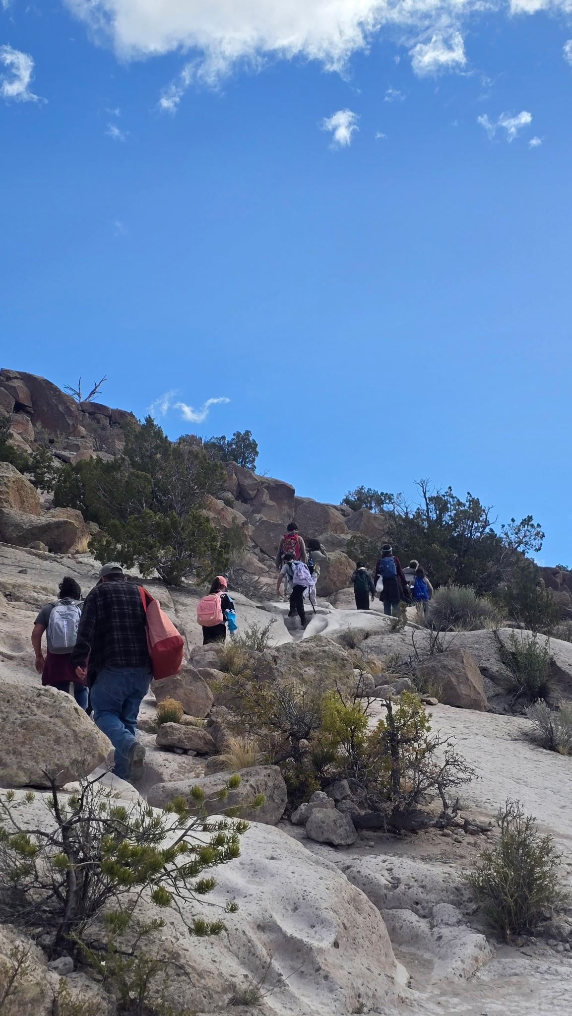 Hikers on a rocky trail under a clear blue sky.
