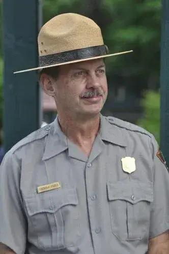 Park ranger in a uniform and hat, standing outdoors.