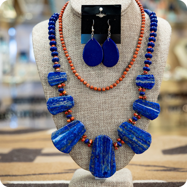 Blue stone necklace and earrings with orange bead accents displayed on a stand.