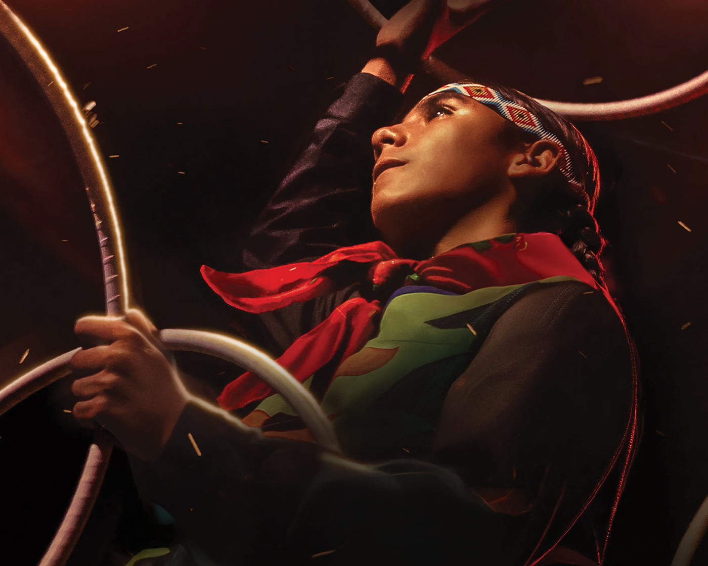 Young person performing a hoop dance, dressed in red and green, with a focused expression.