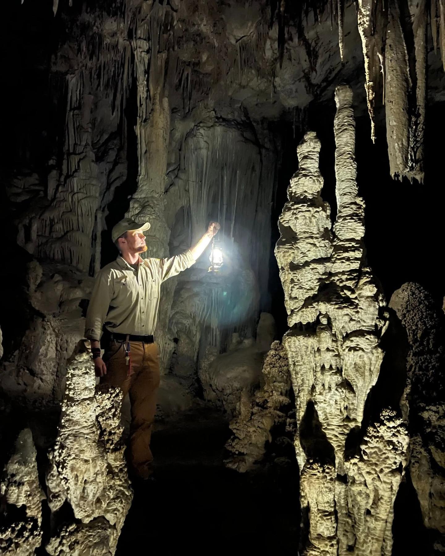 Man holding a light in a dark cave with stalagmites.