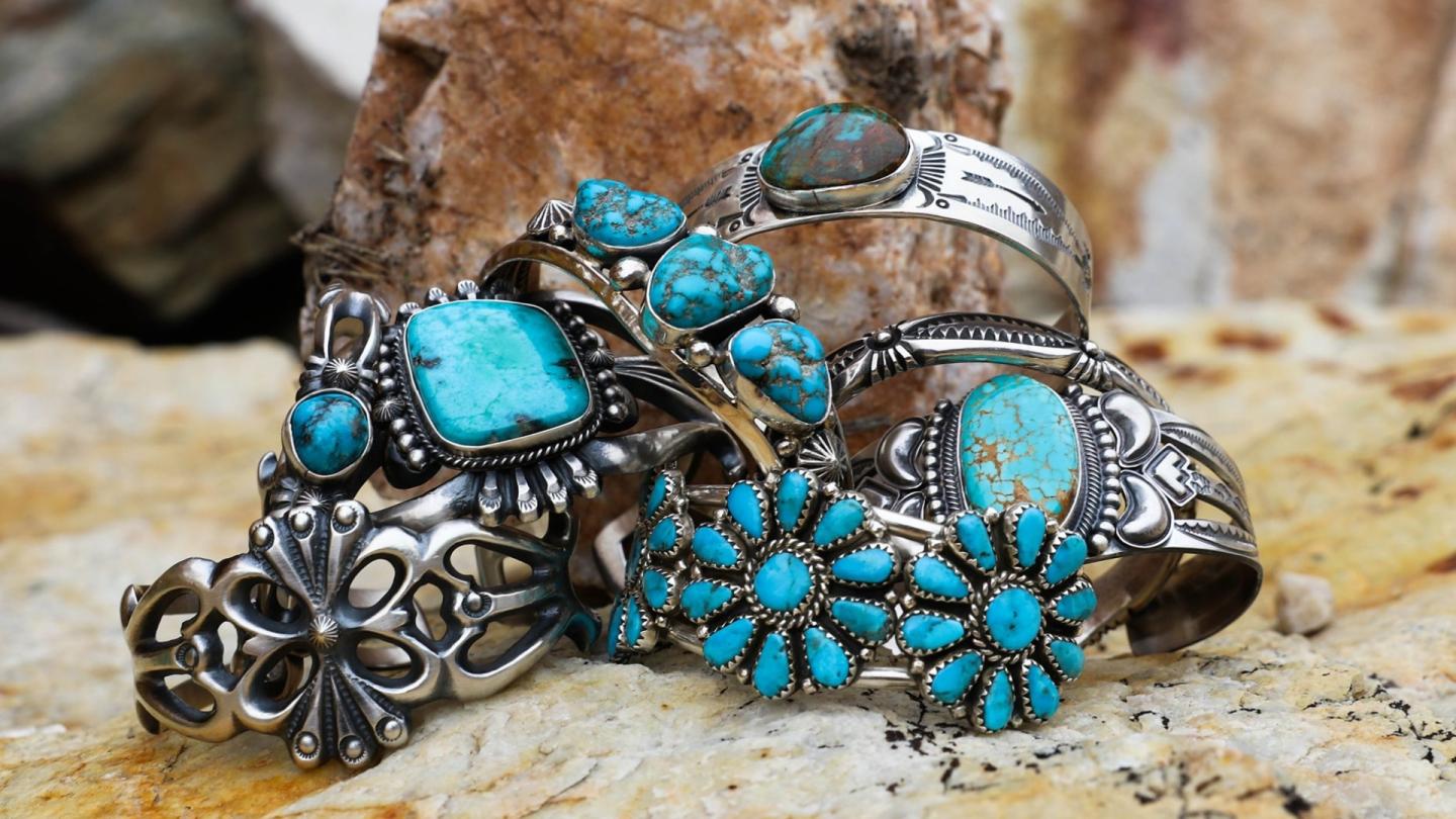 Silver and turquoise jewelry with floral designs on a rustic stone background.