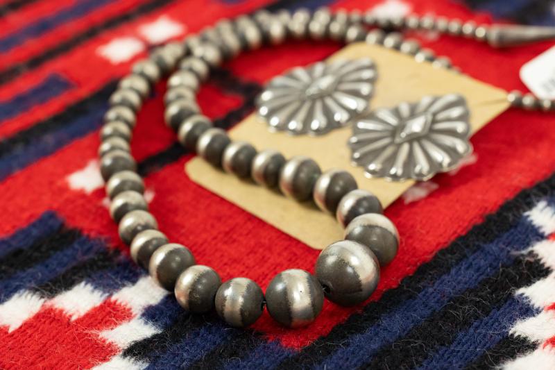 Silver beaded necklace and earrings on a red patterned fabric.