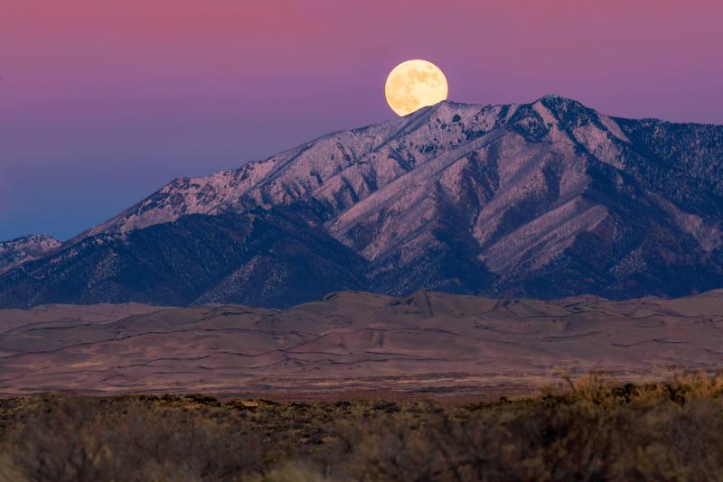 A full moon rising over a ridge with snow