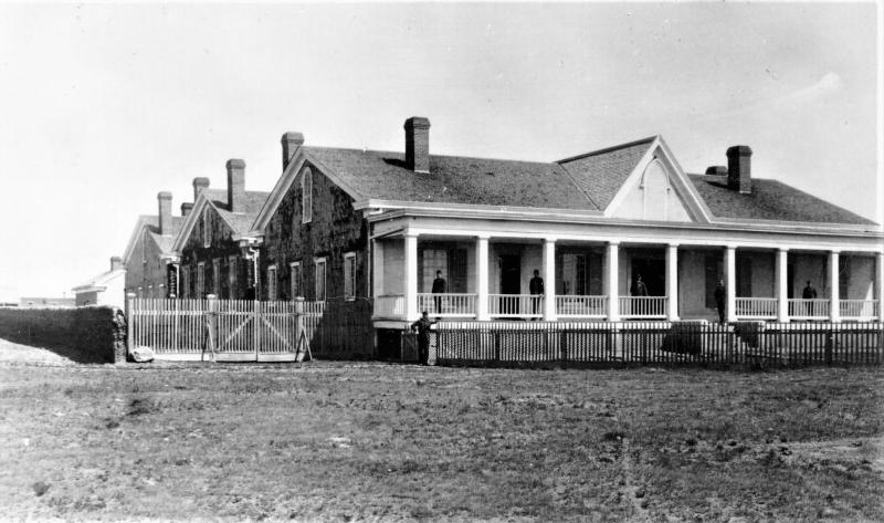 An 1800s image of a frontier hospital with angled roof and covered porch.