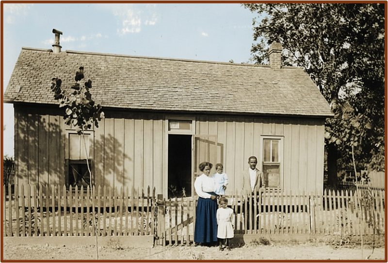 Image of an African American family (man, woman, two children) standing in front of an old home.