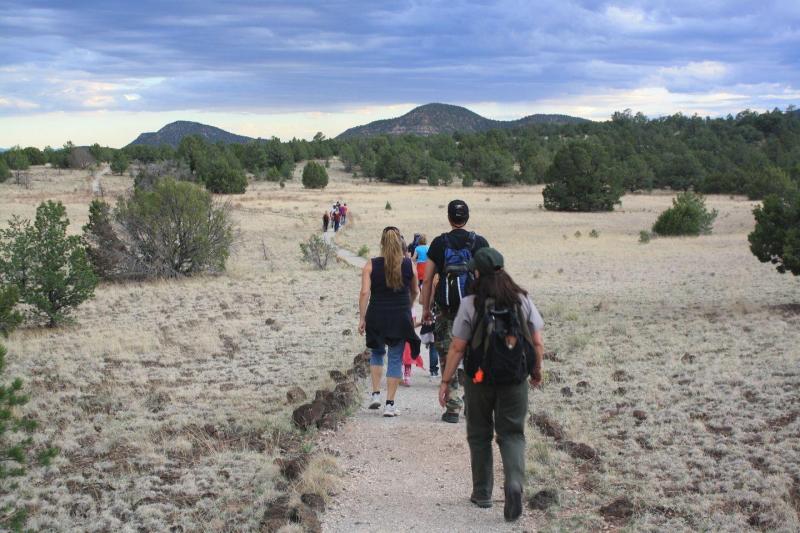 People walking along a dirt trail following a ranger during a ranger-led hike with grass and trees.