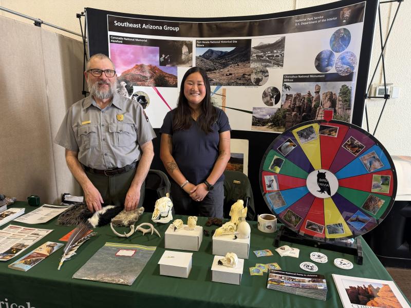 ranger and intern stand at booth with wildlife trivia wheel
