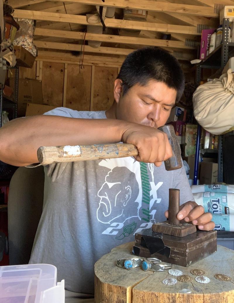 Diné Silversmith McHale Alcott uses a hammer to form a metal bracelet.