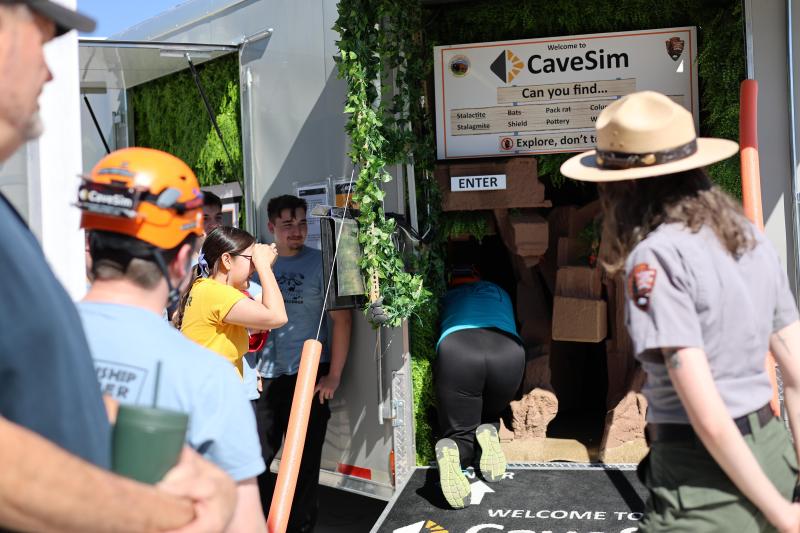 Young students look on as another students crawls into a simulated cave inside a trailer.