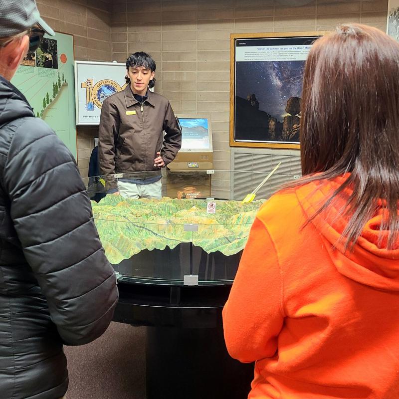 people facing map with NPS staff talking and pointing to large 3d map