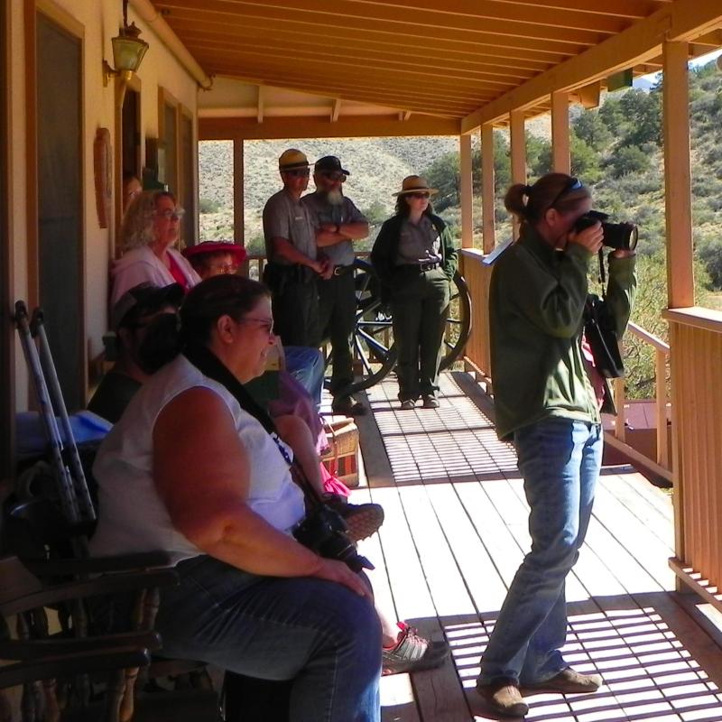 people standing on a porch under an awning with NPS park rangers in green and gray in the background