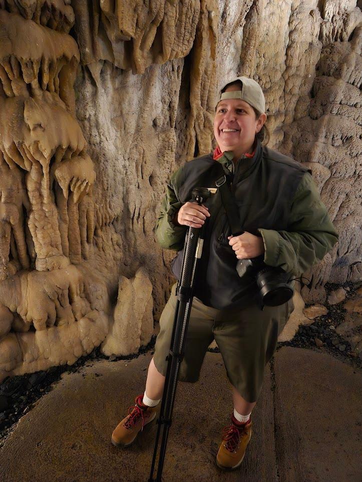 A woman photographer holding a camera in a cave passage.