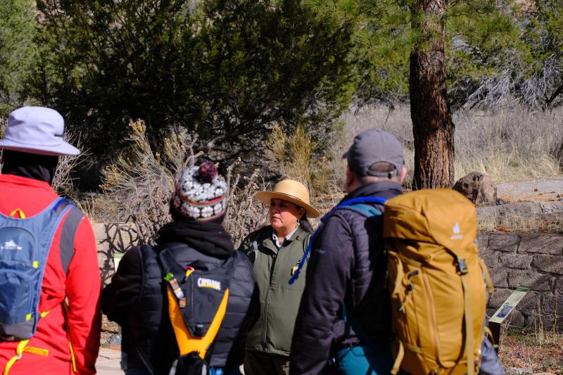 a ranger in a uniform and hat stands talking to visitors