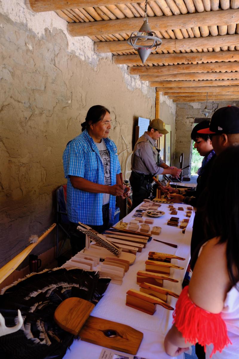 an artist with hand made turkey calls on a table stand talking to visitors.
