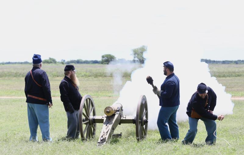 A group of men dressed as 19th century soldiers fire a small cannon.