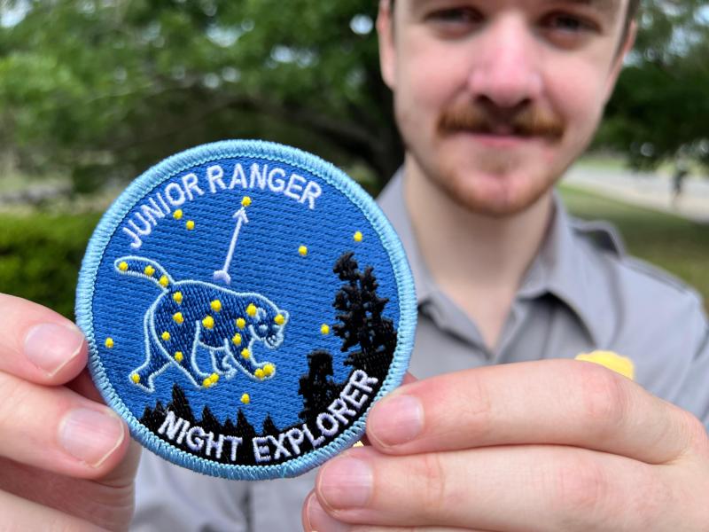 A ranger holds a blue patch with an image of a constellation.