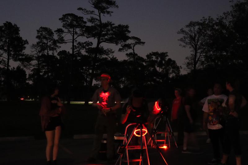 a park ranger talking to a person while standing next to telescopes set up outside on a clear night.