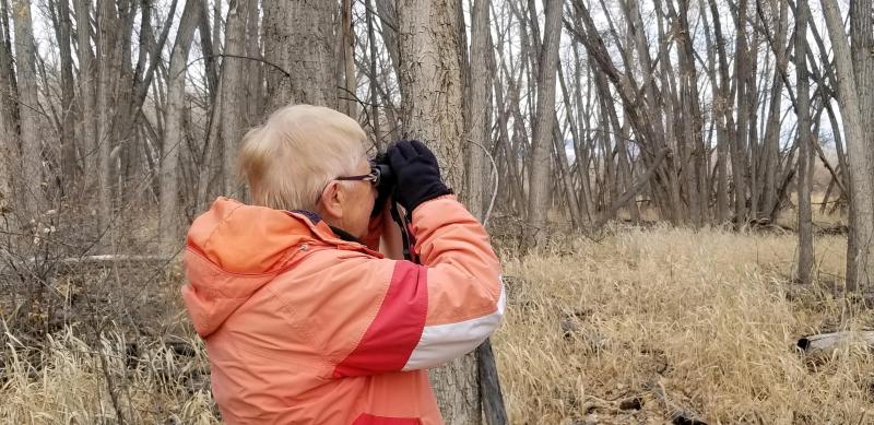 A woman in an orange coat hold binoculars to her eyes looking into the distance.