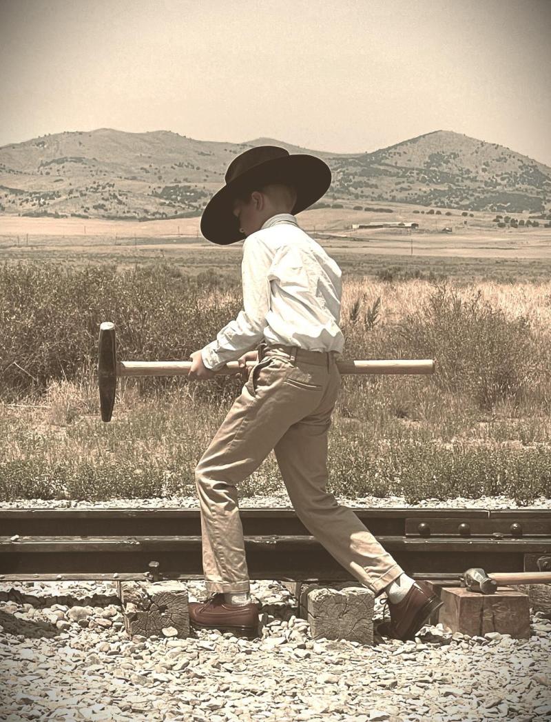 Young Child wearing a cowboy hat, about to hammer a railroad tie with a long handle hammer