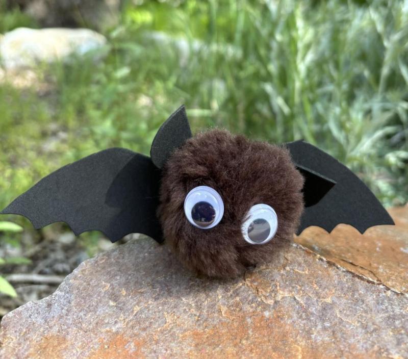 A brown pompom with attached felt wings and ears and googly eyes resembling a stylized bat.