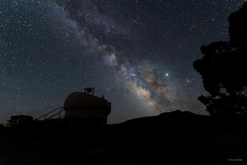 An open observatory dome is silhouetted against a night sky filled with stars and the milky way