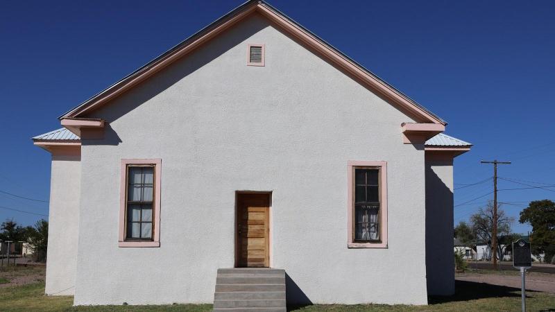A white stucco building with small windows sits in front of a bright blue sky.
