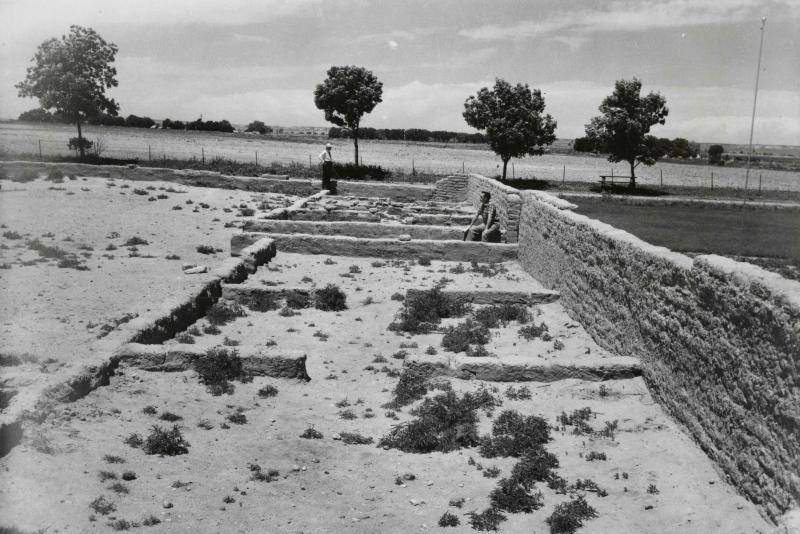 Two men stand or sit on short replica adobe walls outlining the site of Bent's Old Fort