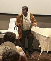 A Native American man standing next to a buckskin that has been prepared.