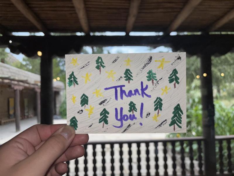 A hand holds out a thank you postcard with trees drawn on it.