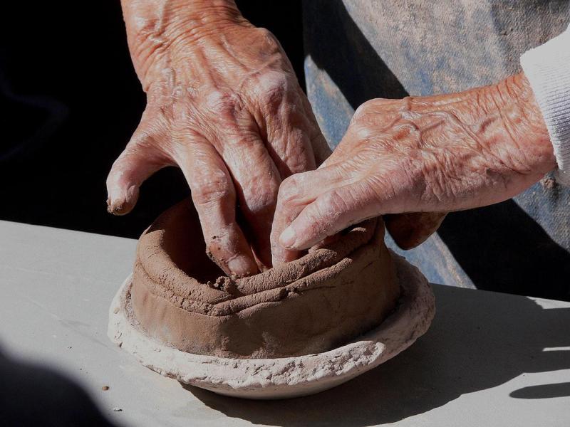 A pair of hands works to shape a brown colored clay into the base of a traditional, handmade pot.