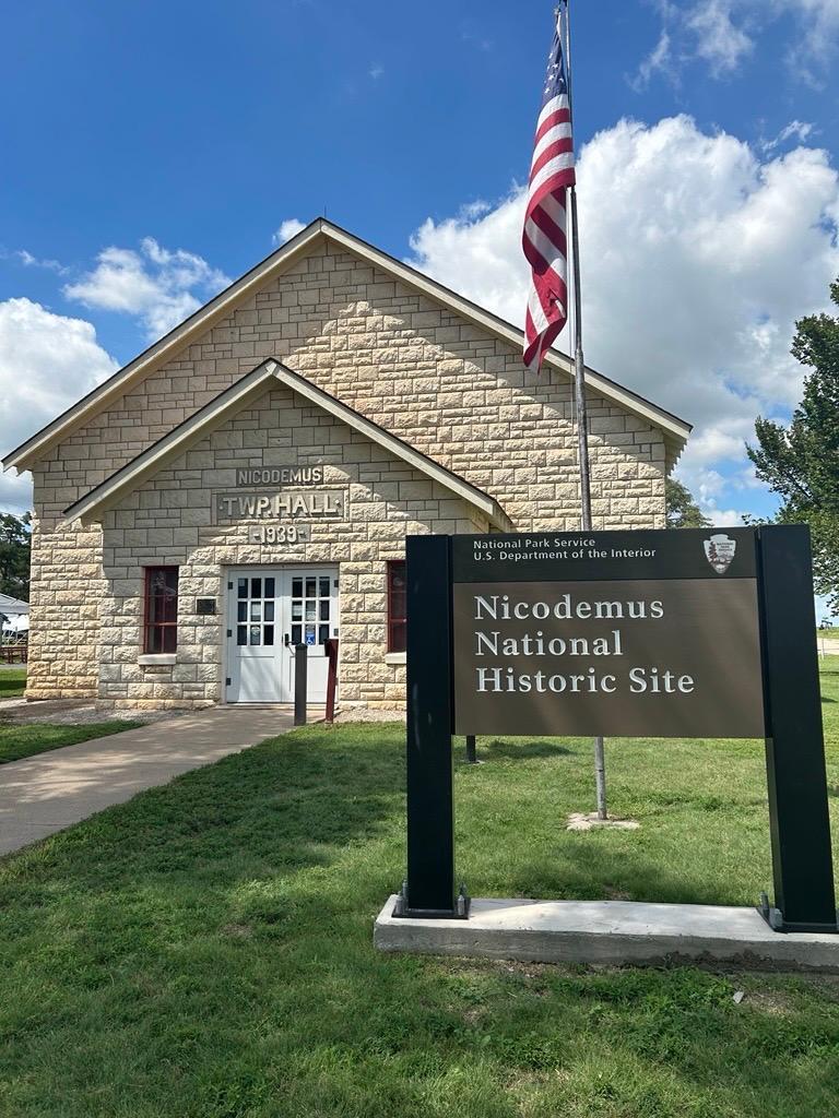 A color photo of a limestone building with a flag pole and sign next to it