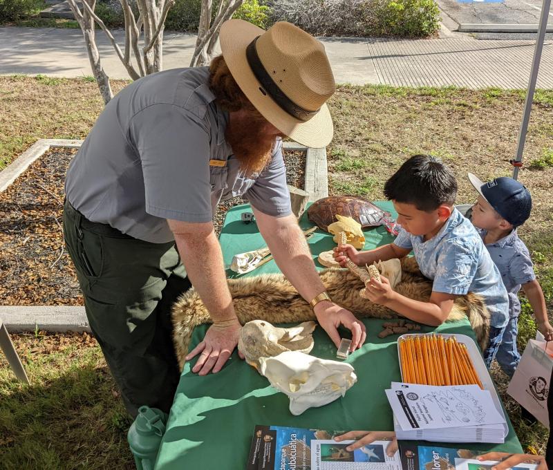A park ranger talks with two kids at a info station