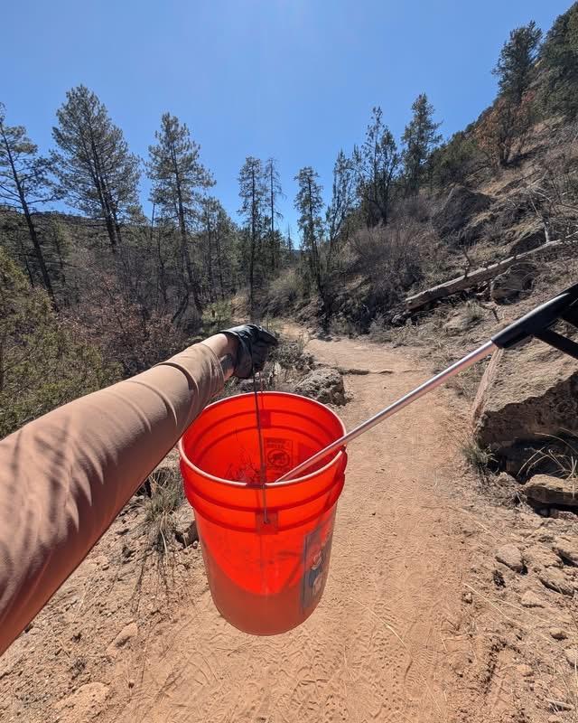 A volunteer holds up an orange trash bucket with trash grabber