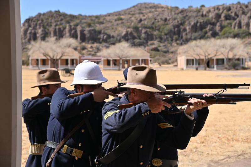 Four people in historical military uniforms and various hats look through rifle sights