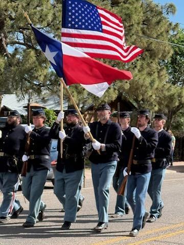 men in historic military uniforms march with American and texas flags