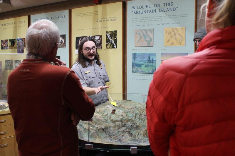 ranger presents over a map with exhibits behind while people watch