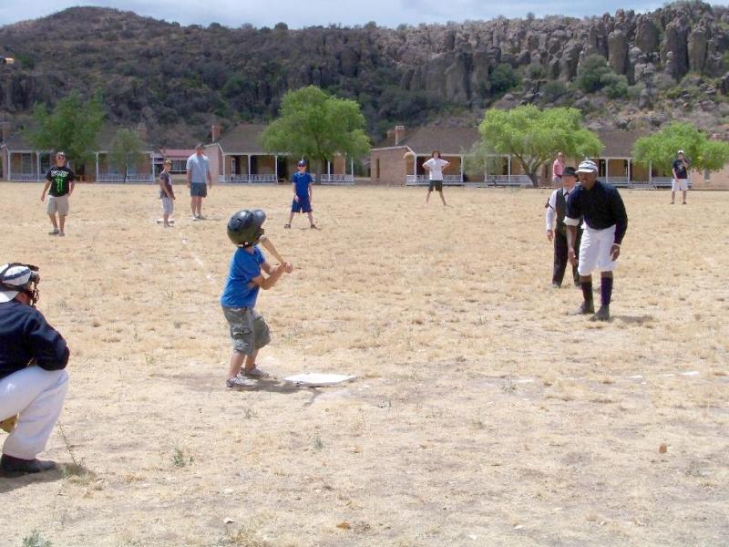 a group of people playing baseball on an arid field with historic fort buildings in the background